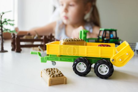 Photo for Cute child plays with farm equipment toys. Business or farming concept, blurred background - Royalty Free Image