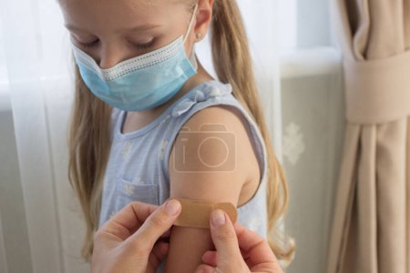 Foto de La niña con una máscara sostiene un brazo con un yeso en la piel. Concepto de vacunación e inmunización - Imagen libre de derechos