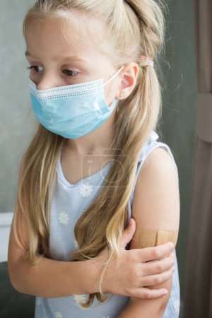 Photo for Little girl in a mask holds an arm with a plaster on the skin. Concept of vaccination and immunization - Royalty Free Image