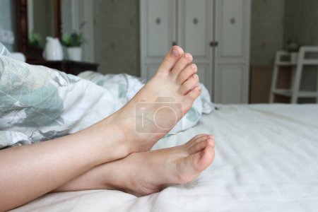 Téléchargez les photos : Pieds sous une couverture légère sur le lit. Concept de santé et de style de vie - en image libre de droit