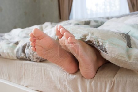 Téléchargez les photos : Pieds sous une couverture légère sur le lit, fond de mise au point doux. Concept de vie saine - en image libre de droit