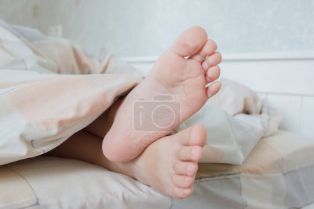 Téléchargez les photos : Pieds sous une couverture légère sur le lit, fond de mise au point doux. Concept de vie saine - en image libre de droit