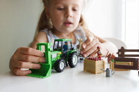 Téléchargez les photos : Mignon enfant joue avec l'équipement agricole jouets. Concept d'entreprise ou d'agriculture, fond flou - en image libre de droit
