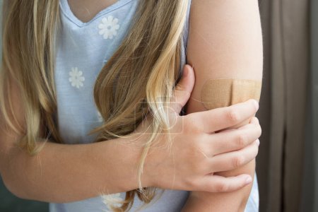 Foto de La niña con una máscara sostiene un brazo con un yeso en la piel. Concepto de vacunación e inmunización - Imagen libre de derechos
