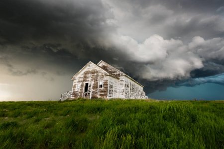 Téléchargez les photos : Old School House se trouve sous un nuage de tempête menacing avec herbe verte luxuriante - en image libre de droit