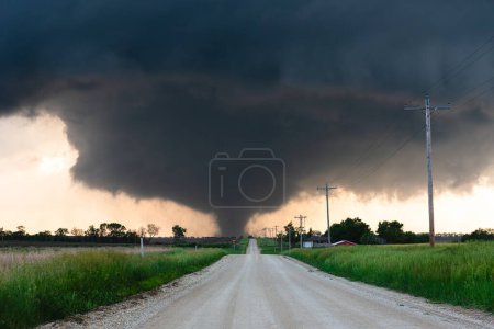 Téléchargez les photos : Tornade effrayante se profile sur une route de terre sous la base sombre de tempête - en image libre de droit