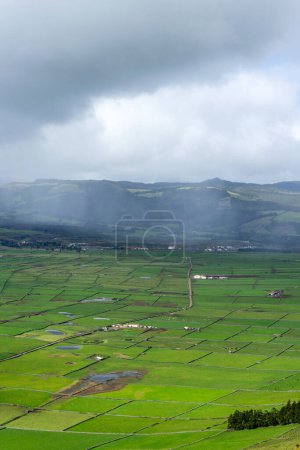 Vista panorámica de exuberantes praderas en la isla de Terceira, Azores, enmarcada por paredes de roca negra, con montañas en el fondo.