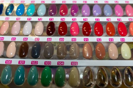 Une exposition d'échantillons d'ongles peints dans un magasin, avec différentes couleurs et dessins. Les échantillons sont soigneusement disposés, mettant en valeur une gamme diversifiée de vernis à ongles, des teintes vives aux nuances subtiles..