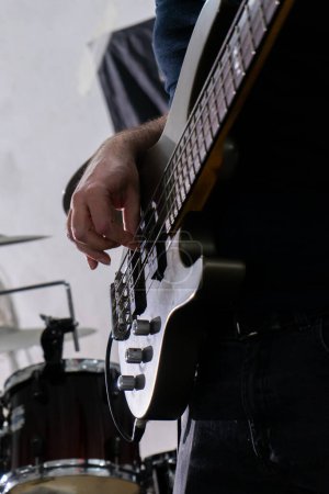 A man playing a bass guitar in a casual setting. He's focused on his instrument, fingers gliding over the strings. His relaxed posture and casual attire suggest a laid-back music session.