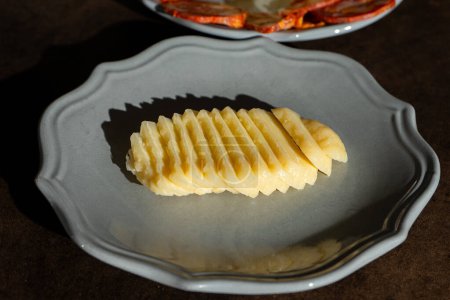 Ein traditioneller Alentejo-Käse, fein säuberlich auf einem Keramikteller geschnitten. Die goldbraune Rinde kontrastiert mit dem cremeweißen Interieur und schafft eine einladende und optisch ansprechende Präsentation.