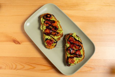 A plate of bruschettas topped with vibrant guacamole and cherry tomatoes sits on a restaurant table. The golden toasted bread contrasts beautifully with the fresh green guacamole and red tomatoes.