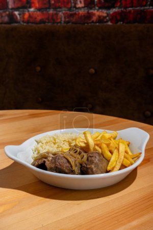 Ein Teller mit geschmorten schwarzen Schweinebäckchen, gepaart mit weißem Reis und knusprigen Pommes frites, steht in einem Restaurant. Dieses traditionelle portugiesische Gericht ist eine warme und herzhafte Mahlzeit.