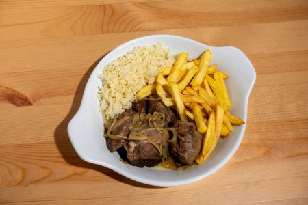 Ein Teller mit geschmorten schwarzen Schweinebäckchen, gepaart mit weißem Reis und knusprigen Pommes frites, steht in einem Restaurant. Dieses traditionelle portugiesische Gericht ist eine warme und herzhafte Mahlzeit.
