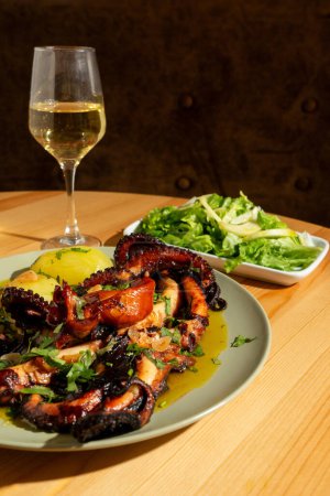 A classic Portuguese dish, "Polvo  Lagareiro," featuring tender octopus with roasted potatoes, garlic, and olive oil. It's presented on a rustic plate, accompanied by a glass of Alentejo white wine. The setting is a warm, inviting restaurant.