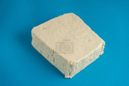 Ein weißer Tofu-Block sitzt vor einem leuchtend blauen Hintergrund, dessen glatte Textur und saubere Kanten einen einfachen, aber markanten Kontrast bilden. Ideal für Gesundheitsthemen und pflanzliche Lebensmittel.