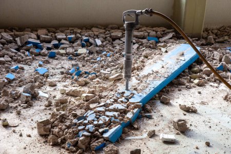 A pneumatic jackhammer demolishes walls and floor, creating a cloud of dust and debris. The powerful tool showcases intense construction work in progress.