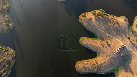 Photo for Aerial view of Monte Novo Dam in vora at sunset, showcasing serene water, surrounding greenery, and the golden hues of the setting sun casting a tranquil ambiance. - Royalty Free Image