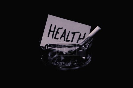 pedazo de papel con la escritura "salud" quema debido al humo del cigarrillo en un cenicero, concepto de "fumar mata"