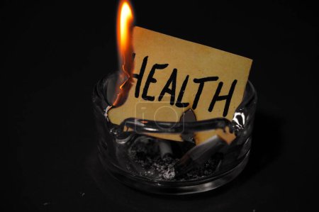 Photo for Piece of paper with the writing "health" burning due to cigarette smoke in an ashtray, concept of "smoking kills" - Royalty Free Image