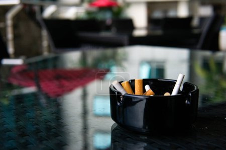 lit cigarette in a black glass ashtray on a black mirror surface