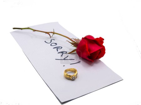 Note of apology with weeding ring and rose on wood