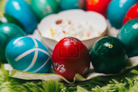 Experimente la elegancia de la Pascua ortodoxa con una encantadora muestra de requesón con fruta seca, rodeado de huevos de mármol de colores. Esta foto emana riqueza cultural y encanto festivo.