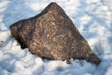 A large stone lies in the snow, winter and sunny day. High quality photo