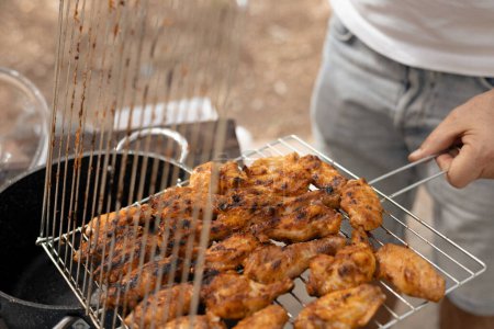 Photo for A man on a picnic holds a net with appetizing ready-to-grill meat and lays it out with tongs, a hot spring day. High quality photo - Royalty Free Image