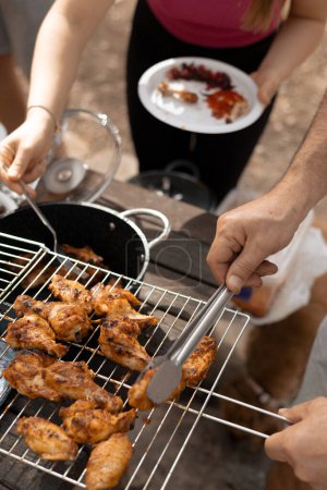 Photo for A man on a picnic holds a net with appetizing ready-to-grill meat and lays it out with tongs, a hot spring day. High quality photo - Royalty Free Image