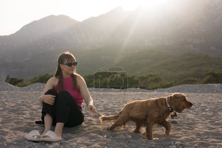 Photo for Beautiful young girl and her cocker spaniel dog having fun on the beach on a hot spring day, mountains in the background, sunset. High quality photo - Royalty Free Image