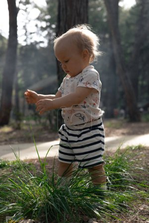 Photo for Adorable little blonde girl playing with grass in the forest park on a hot sunny day. High quality photo - Royalty Free Image