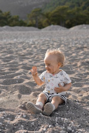 Beautiful little blonde girl in shorts and a T-shirt plays on the beach, happy sunny spring day. High quality photo