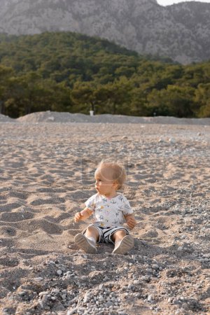 Photo for Beautiful little blonde girl in shorts and a T-shirt plays on the beach, happy sunny spring day. High quality photo - Royalty Free Image