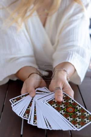 Frau im hellen Outfit liest Tarotkarten auf einem Tisch in einem Café, Nahaufnahme
