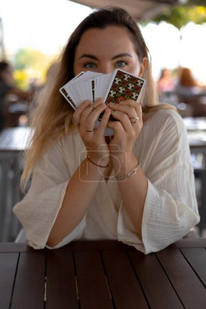 Photo for Young beautiful blonde Woman in a light outfit reads Tarot cards on a table in a cafe - Royalty Free Image