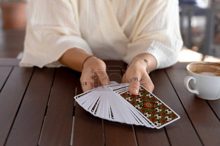 Woman in a light outfit reads Tarot cards on a table in a cafe, close-up view
