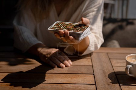 Frau im hellen Outfit liest Tarotkarten auf einem Tisch in einem Café, Nahaufnahme