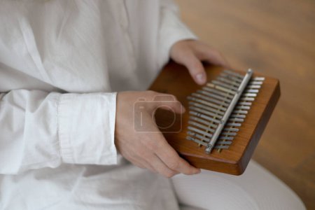 Kalimba in the hands of a young woman musician in white clothes sitting on the floor at home