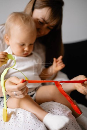 Photo for Cute baby in mothers arms playing games developing hand motor skills at home - Royalty Free Image