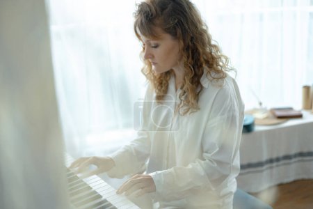 Photo for Young woman in white clothes sitting and playing an electronic piano. - Royalty Free Image