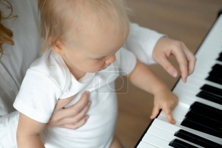 Photo for Little toddler girl sits on mothers hands at the piano and learns to play. Music class - Royalty Free Image