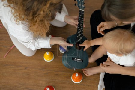 Photo for Music lesson for a little toddler girl, bells, ukulele, guitar and other musical instruments - Royalty Free Image