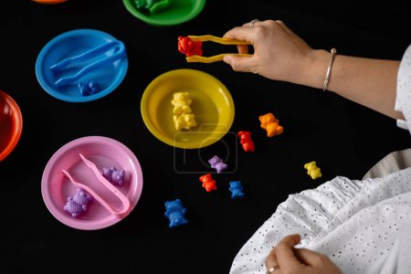 Photo for Development of fine motor skills for children using tweezers and small toys. black background - Royalty Free Image