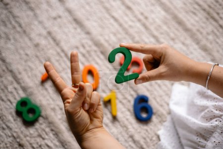 Photo for Young woman holding multi-colored wooden numbers in her hands to teach children to count - Royalty Free Image