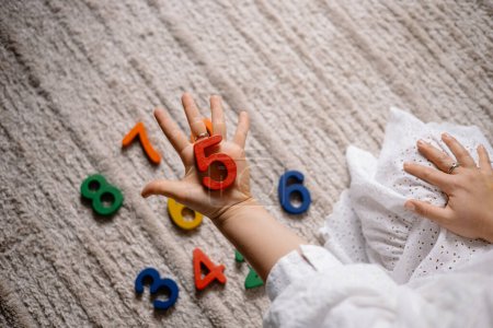Photo for Young woman holding multi-colored wooden numbers in her hands to teach children to count - Royalty Free Image