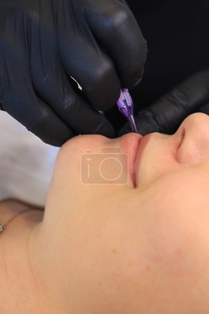 Young woman undergoing procedure of permanent makeup in tattoo salon, closeup