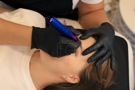 Young woman undergoing procedure of permanent makeup in tattoo salon, closeup