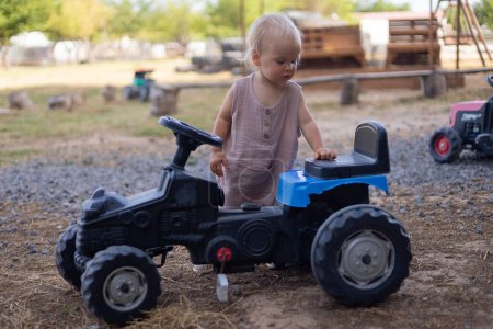 Cute blonde little girl playing with miniature tractor on eco farm