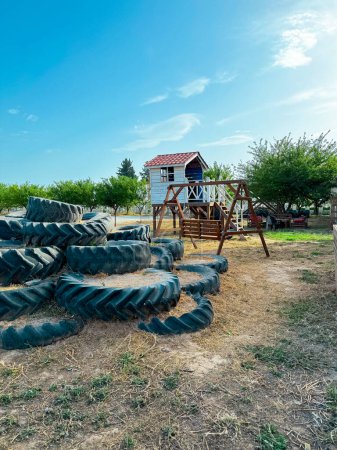 childrens playground made of wood in eco style, wooden house and tractor tires, bright blue sky