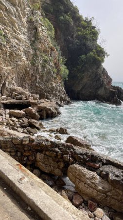 Beautiful puff rocks on pebble public stone beach. Rafailovici resort towns. Montenegro. Adriatic Sea. Summer sunny day. Seaside vacation concept. High quality photo
